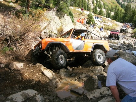 1995 Ford Bronco - An off-road vehicle navigates a challenging rocky path, with spectators and other vehicles on the trail.