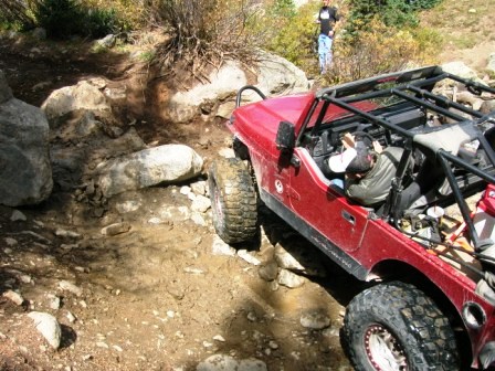 1995 Ford Bronco - A red off-road vehicle navigates a challenging rocky trail, with a person standing in the background.