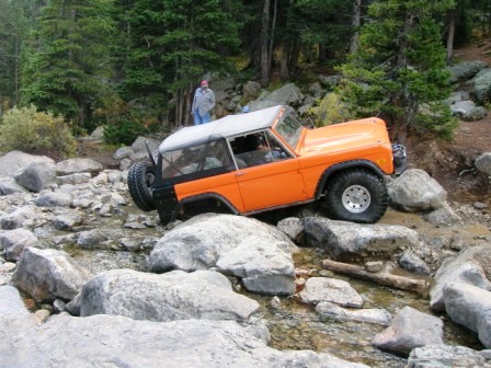 1995 Ford Bronco - An orange 1978 Ford Bronco traverses a challenging rocky terrain with a person standing in the background.