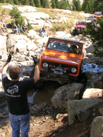 1995 Ford Bronco - An off-road vehicle navigates a challenging rocky course, with spectators and other vehicles in the background.