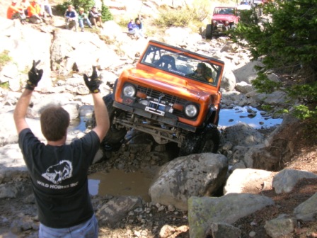 1995 Ford Bronco - An orange Ford Bronco navigates a challenging rocky terrain, with spectators watching from a hillside.