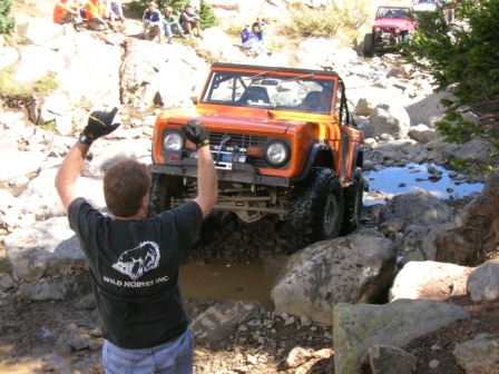 1995 Ford Bronco - A 1970s Ford Bronco navigates a challenging rocky course, guided by a spotter, with another vehicle visible in the background.