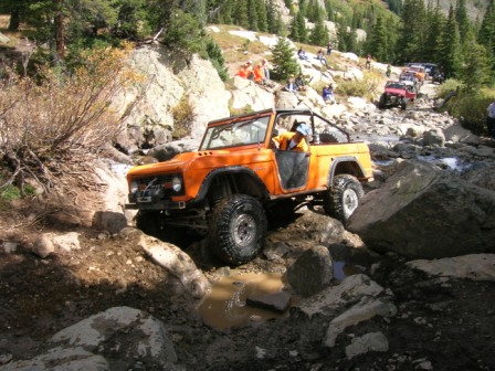 1995 Ford Bronco - A first-generation Ford Bronco tackles a challenging rocky trail, with a line of other off-road vehicles following.