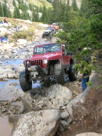 1995 Ford Bronco - A convoy of Jeeps traverses a challenging rocky terrain on a mountain trail.