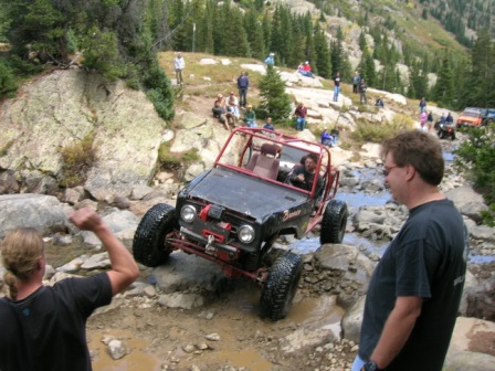 1995 Ford Bronco - Spectators watch as an off-road vehicle tackles a challenging rocky stream during an outdoor event.