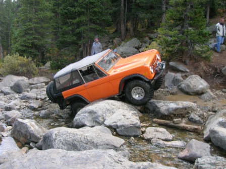 1995 Ford Bronco - This orange Ford Bronco navigates a challenging rocky trail, demonstrating its off-road capabilities.