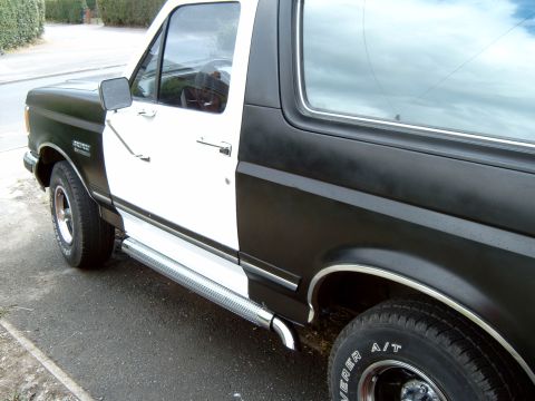 1989 Ford Bronco - A two-tone black and white Ford Bronco is viewed from the side, highlighting its running boards and tires.
