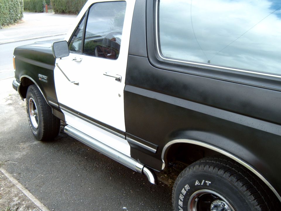 Two-tone black and white Ford Bronco, side view, showing chrome running boards and A/T tires