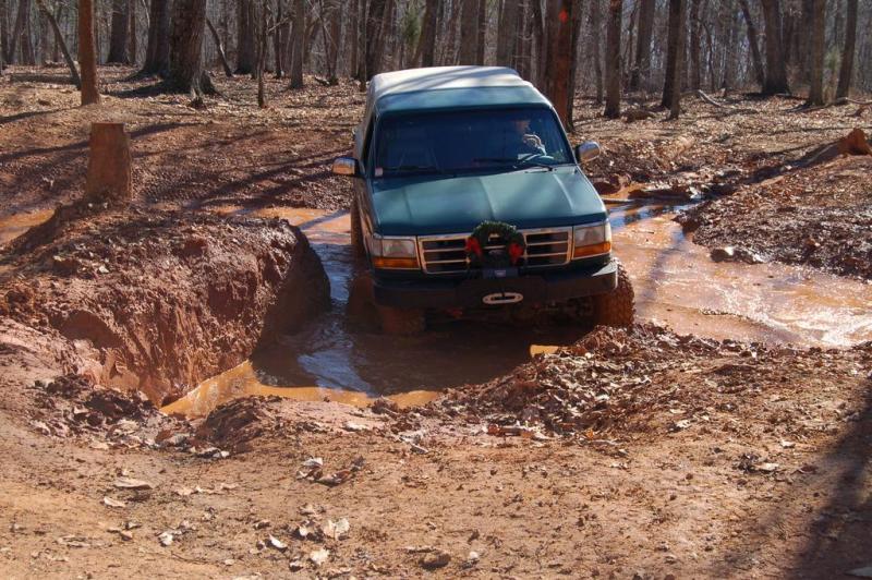 Green SUV navigating a muddy trail with a wreath on the grille