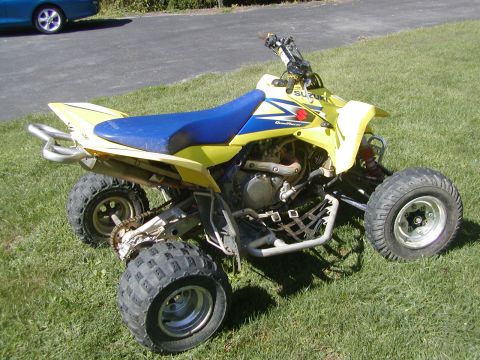 1991 Ford Bronco - This Suzuki QuadRacer ATV features a yellow body with a blue seat and is shown from a three-quarter front view on a grassy lawn.
