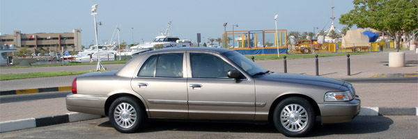 Gold 2007 Mercury Grand Marquis parked on pavement near a marina with boats in the background