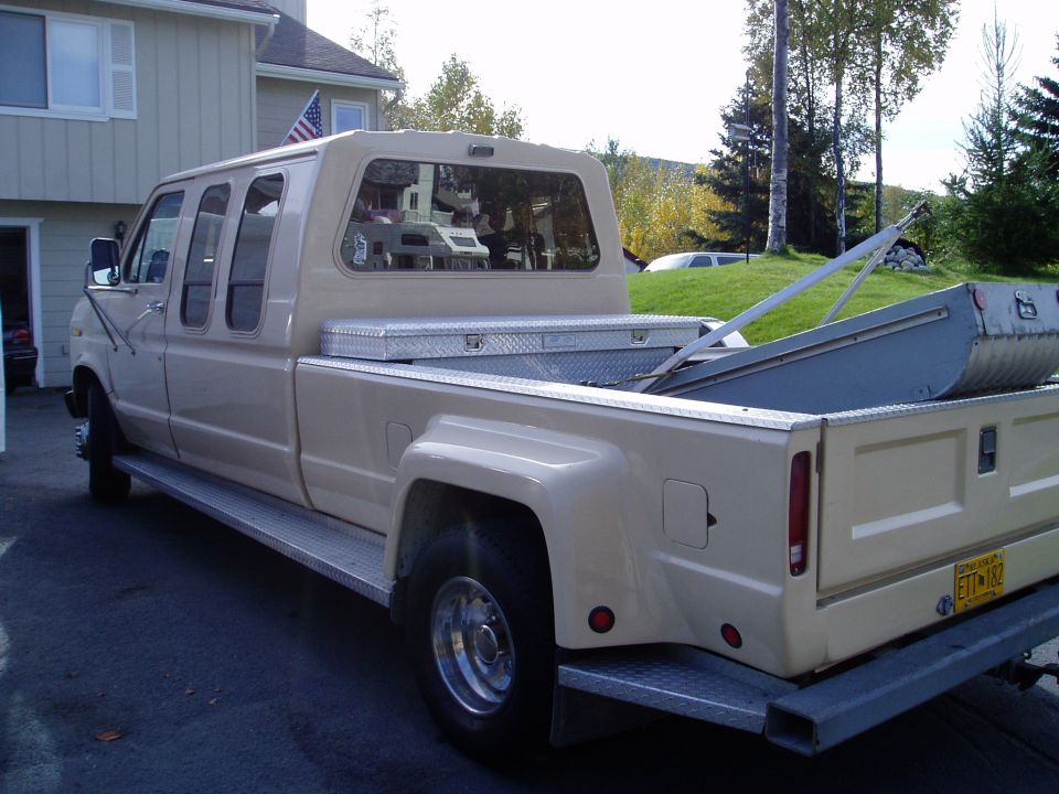 Extended cab pickup truck, tan, with a camper shell, toolbox, and a boat or sled in the bed