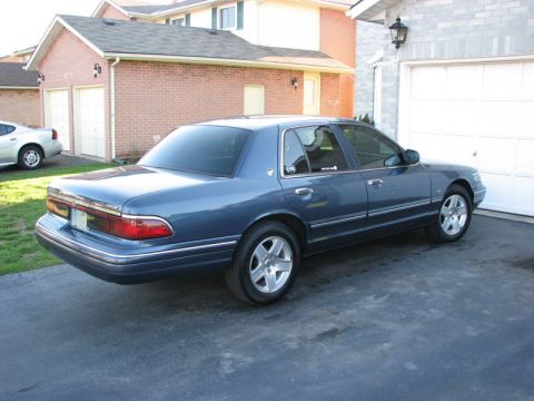 1985 Mercury Grand Marquis - A blue sedan is parked in a driveway in front of a residential garage.
