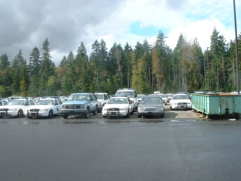 2000 Ford Crown Victoria - A fleet of vehicles, including several police cruisers and a pickup truck, are parked in an outdoor lot.