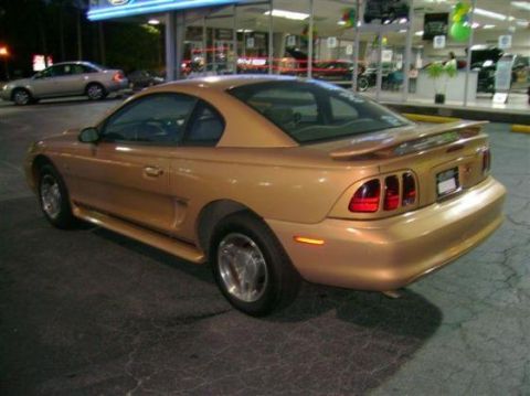 1991 Ford Bronco - This gold coupe, likely a 1994 model, is shown from the rear quarter angle, highlighting its distinctive spoiler and taillight design.