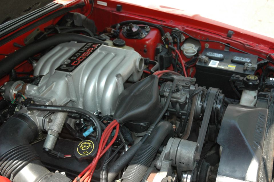 1993 Ford Mustang Cobra engine bay, red exterior paint, silver intake manifold with '5.0 LITER COBRA' text, black hoses, red spark plug wires, battery