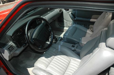 1993 Ford Mustang - The interior of a red vehicle features gray leather seats and a dashboard with a steering wheel.