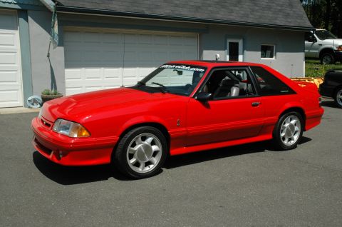 1993 Ford Mustang - A red 1993 Ford Mustang is parked in front of a garage with its sunroof open.