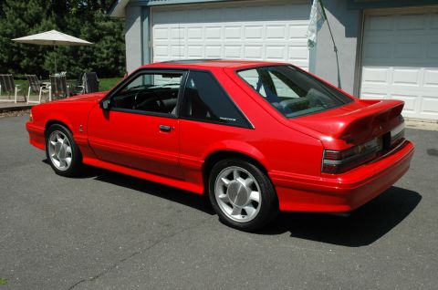 1993 Ford Mustang - A red 1993 Ford Mustang coupe is viewed from the rear three-quarter angle, parked in a driveway.