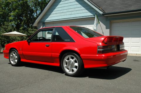 1993 Ford Mustang - A bright red 1993 Ford Mustang is captured from a three-quarter front view, parked in front of a residential garage.