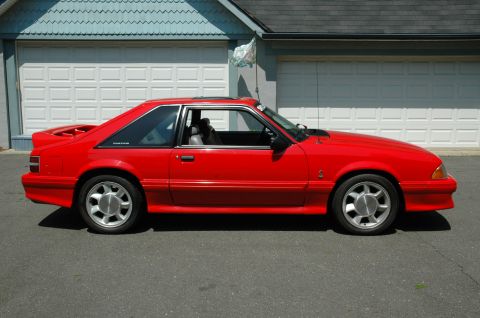 1993 Ford Mustang - Side view of a red 1993 Ford Mustang Cobra parked on asphalt in front of a garage.