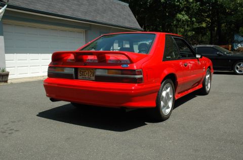1993 Ford Mustang - A red 1993 Ford Mustang is parked in front of a garage, with another car visible in the background.