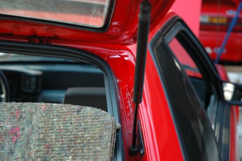 1993 Ford Mustang - Close-up of a red car's interior door frame and strut, with another vehicle in the background.