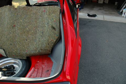 1993 Ford Mustang - The interior of a car trunk is visible, with a spare tire and jack stored below a lifted carpeted panel.