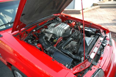 1993 Ford Mustang - The engine bay of a red 1993 Ford Mustang is visible with the hood raised, revealing the V8 engine.