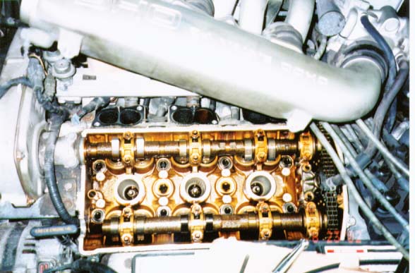 Exposed DOHC cylinder head with camshafts and timing chain, valve cover removed, heavy oil varnish visible