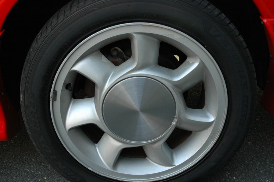 Red car's front passenger side wheel, silver alloy with five spokes and a brushed metal center cap