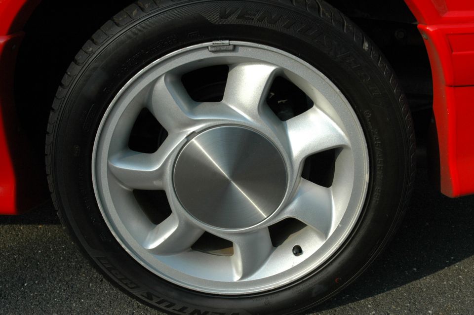 Close-up of a silver 5-spoke wheel with a brushed metal center cap on a red car