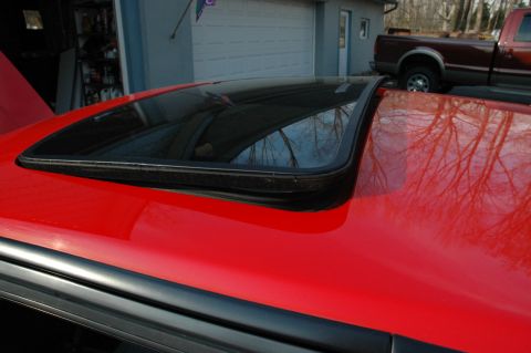 1993 Ford Mustang - Close-up of a red car's sunroof, with a pickup truck visible in the background.