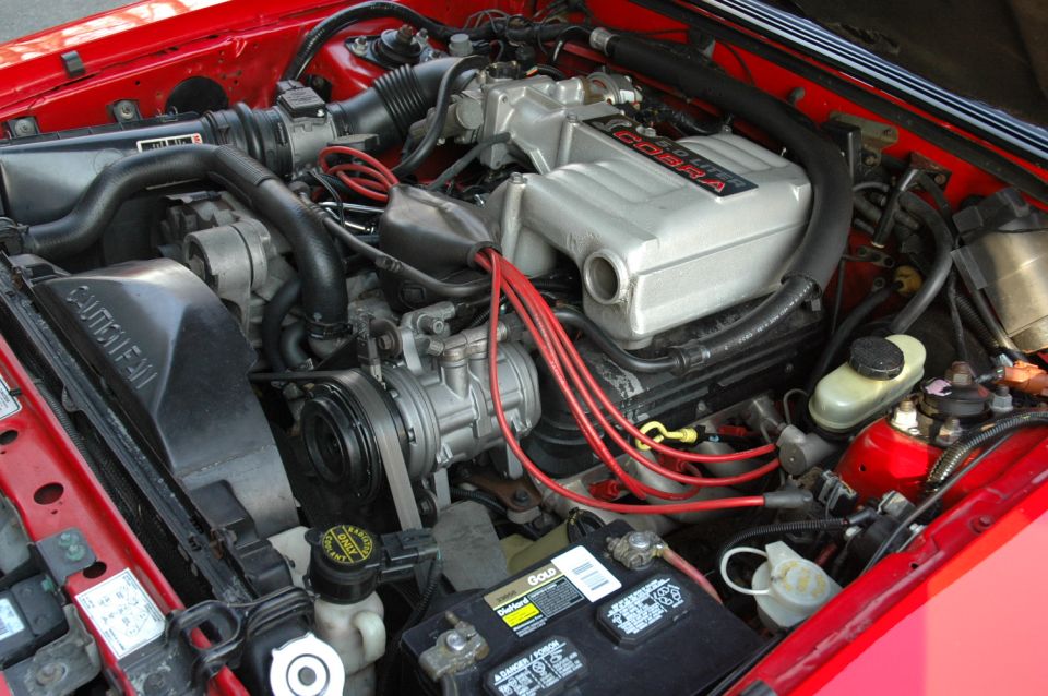 Mustang engine bay with Cobra valve cover, red plug wires, and DieHard battery