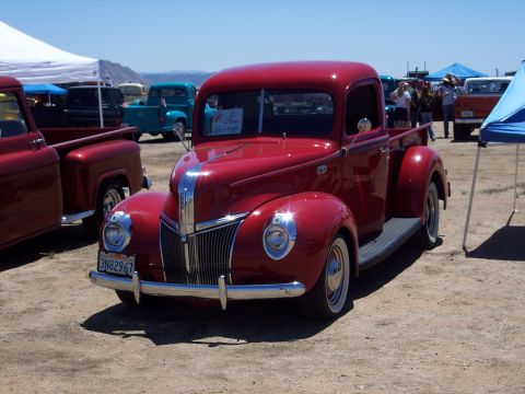 1981 Kenworth W900A - A classic red pickup truck is parked outdoors at an event with other vehicles and tents in the background.