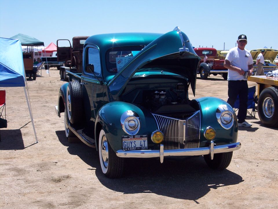 Teal 1940s Ford pickup with hood open showing V8 engine at outdoor truck show
