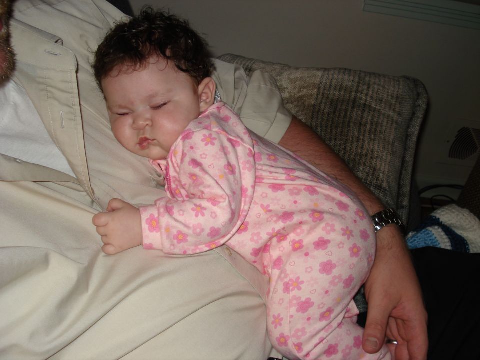 Baby in pink floral pajamas sleeps on an adult's shoulder