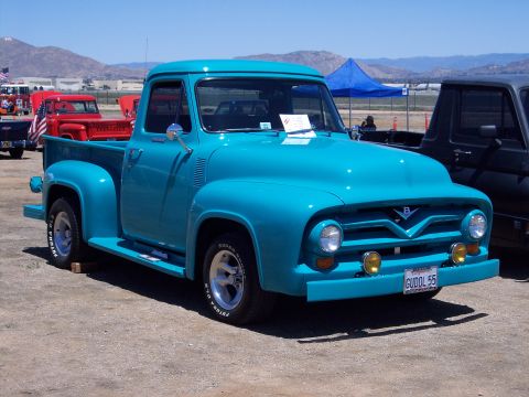 1981 Kenworth W900A - A bright turquoise 1955 Ford F-100 pickup truck is parked outdoors, with other vehicles and tents in the background.