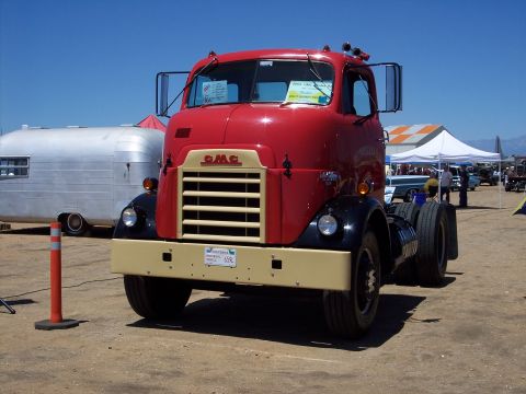 1981 Kenworth W900A - A classic red GMC truck is parked at an outdoor event, with a silver trailer to its left.