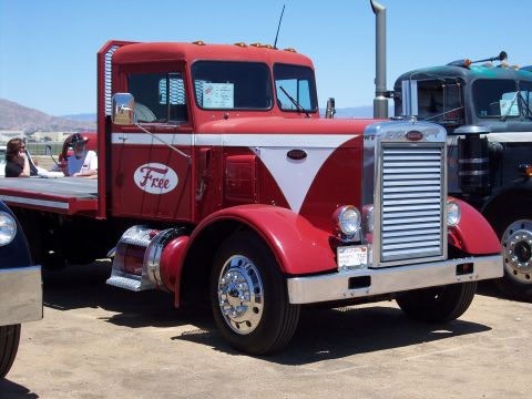 1981 Kenworth W900A - A red flatbed truck with a white stripe and 'Free' logo is parked next to another truck.