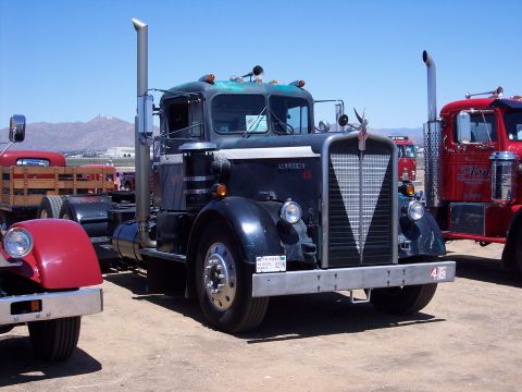 1981 Kenworth W900A - A dark blue semi-truck is parked next to a red one under a clear blue sky.