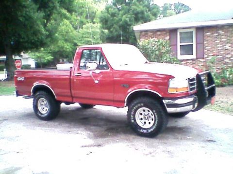 1992 Ford F-150 - Red Ford F-Series regular-cab short-bed pickup viewed from the passenger side on a concrete driveway, with a black tube grille guard on the…