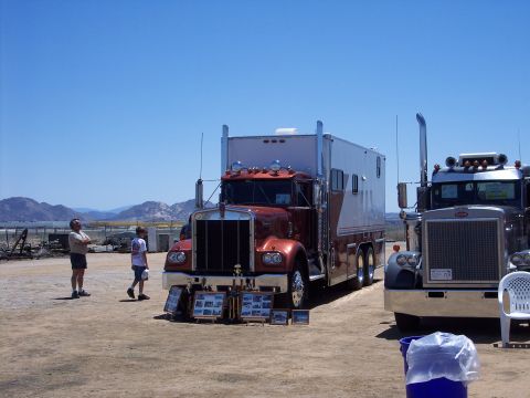 1981 Kenworth W900A - Two large trucks are displayed outdoors under a clear blue sky, with mountains in the background.