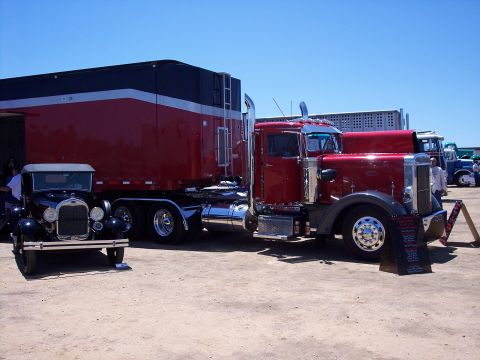 1981 Kenworth W900A - A red semi-truck and a black vintage car are displayed outdoors under a clear blue sky.