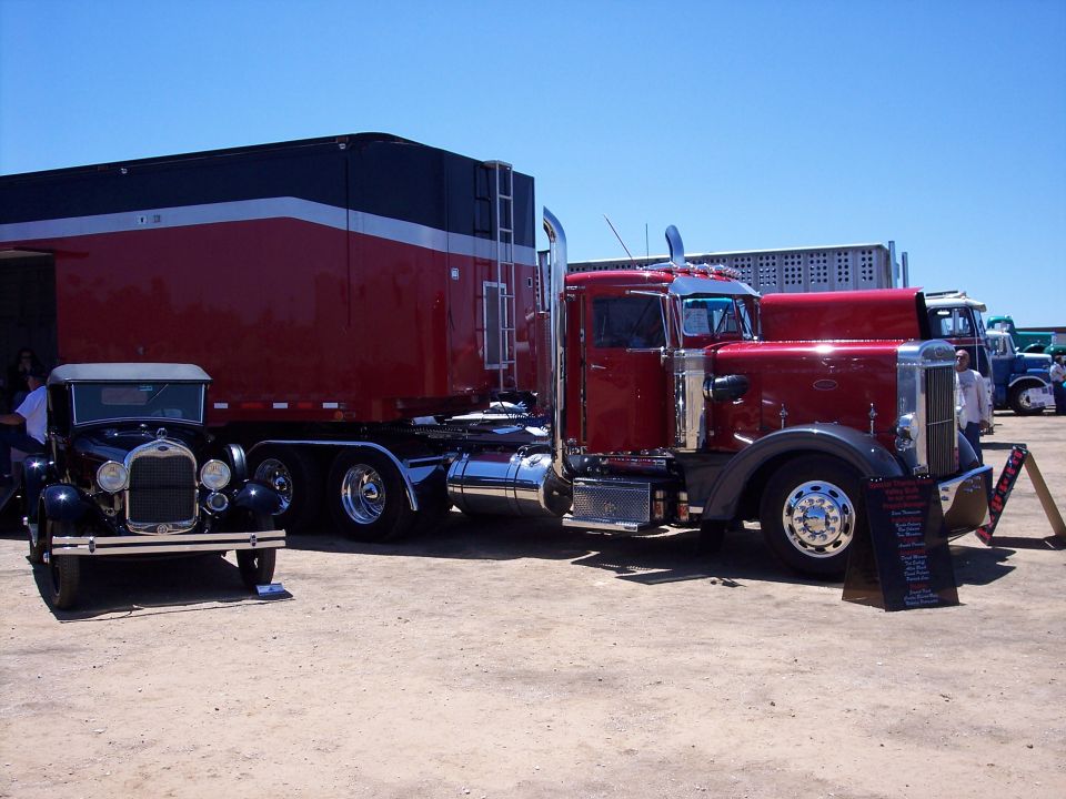 Red vintage Peterbilt tractor with trailer at a truck show beside a black Model A sedan