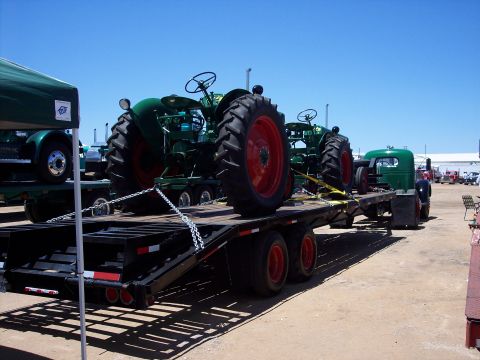 1981 Kenworth W900A - Two vintage green tractors are transported on a flatbed trailer under a clear blue sky.