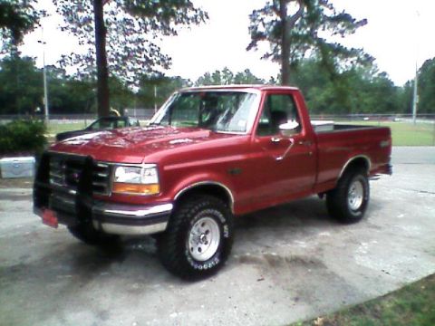 1992 Ford F-150 - Red Ford F-Series regular-cab short-bed 4x4 pickup shot from the front driver's-side three-quarter angle on a concrete pad. It wears a blac…