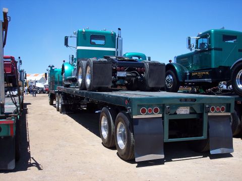 1981 Kenworth W900A - Multiple vintage trucks are displayed on a flatbed trailer under a clear blue sky.