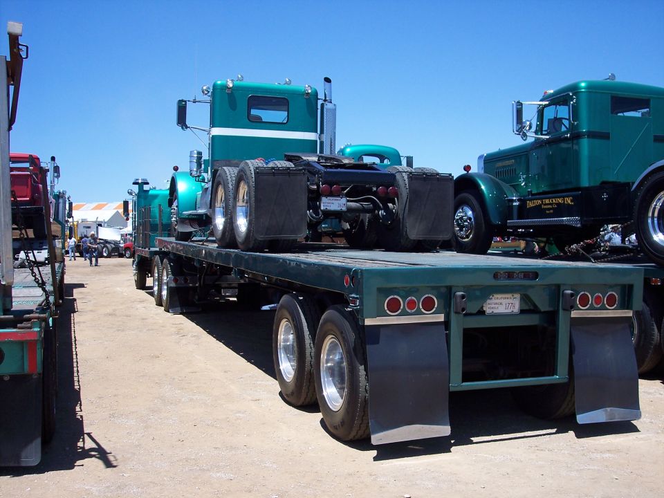 Green conventional semi tractor with matching flatbed trailer at a truck show on a dirt lot