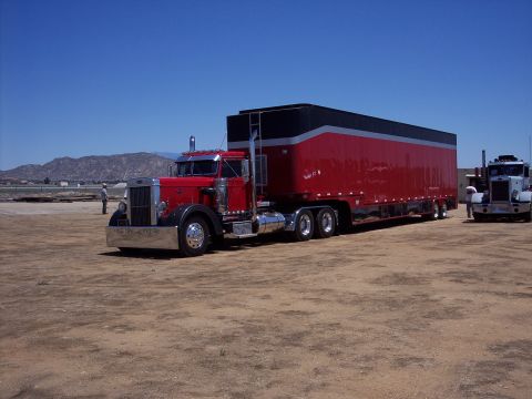 1981 Kenworth W900A - Two semi-trucks are parked in an outdoor lot under a clear blue sky.